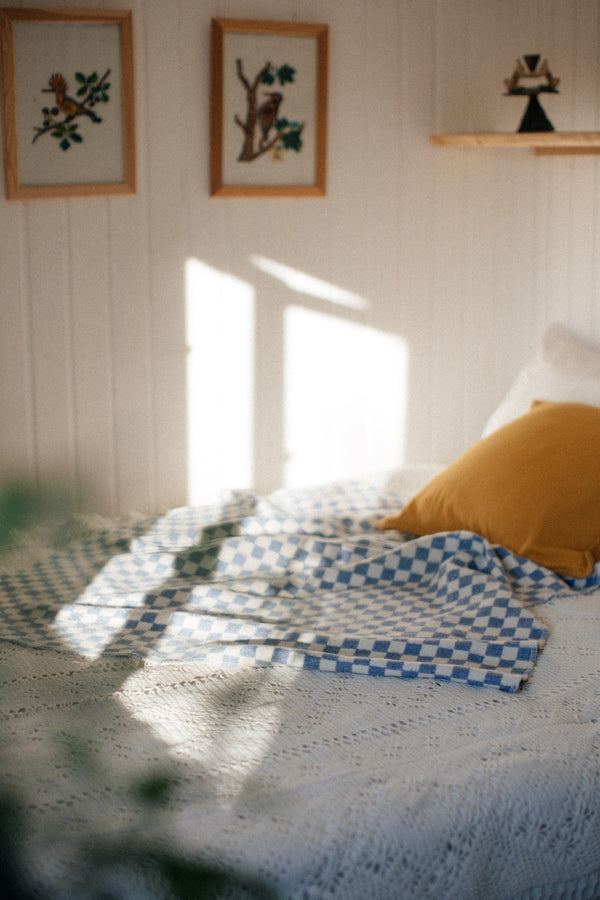 Blue checkered blanket on a bed, sun light of the wall with some frames