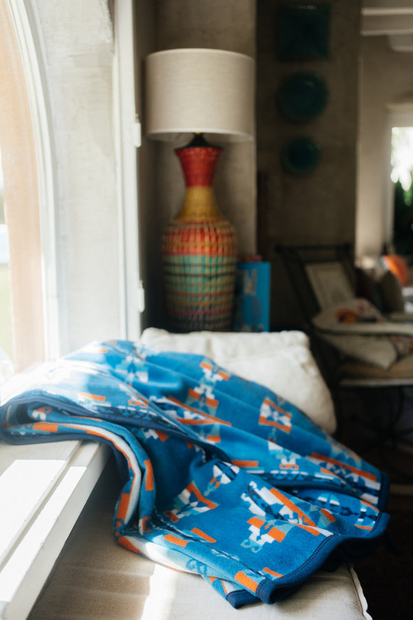 Blue mother and child blanket on a windowsill seat with a beautiful tall lamp with orange yellows and greens raffia like texture