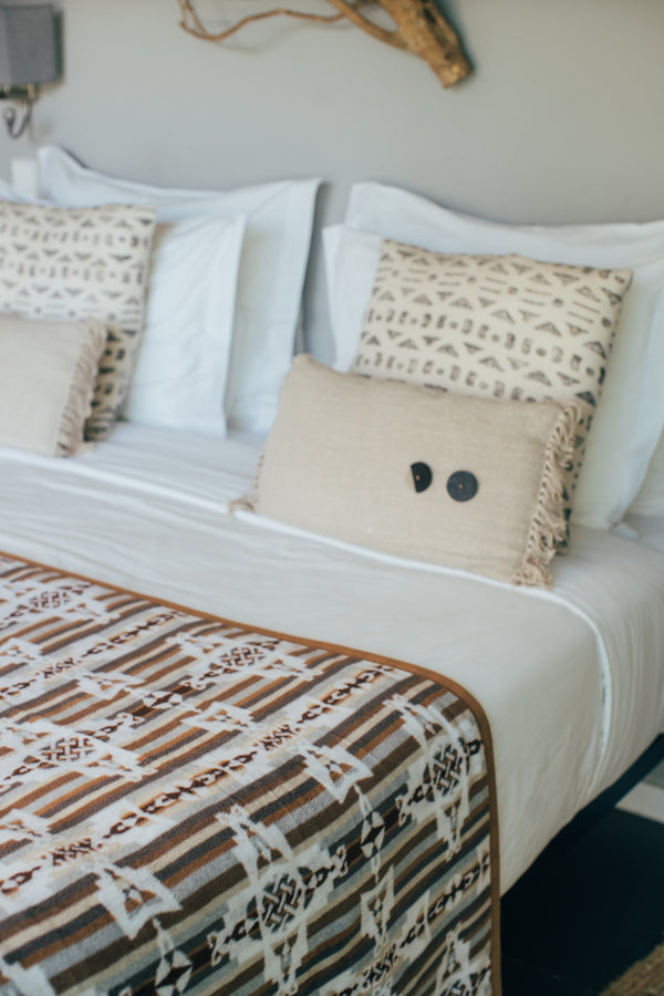 Blanket neatly spread over the surface of a bed with white sheets and white and beige pillows