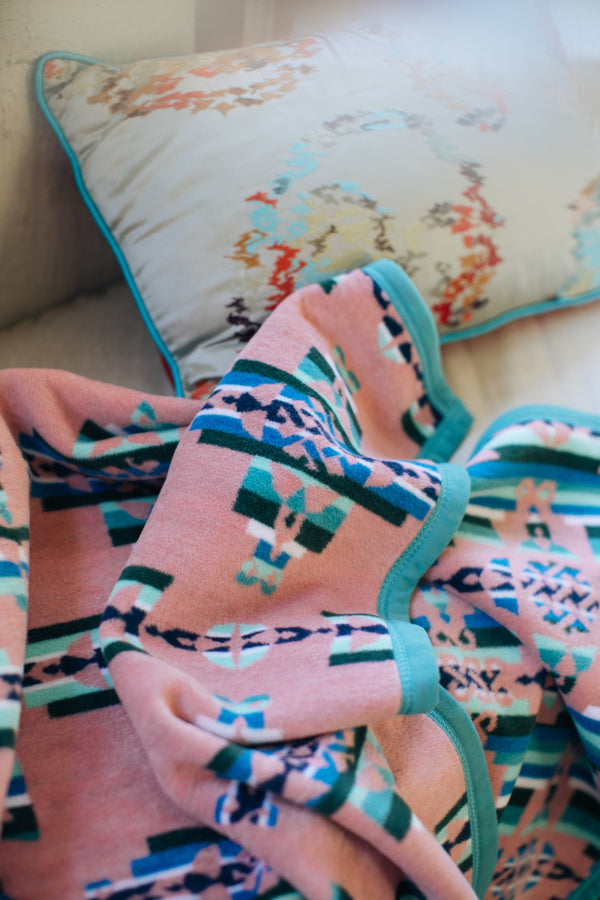 Mother and child geometric pattern in muted pink, blue and green next to a white cushion with coral and blue sea tones