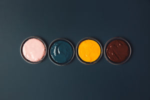 Pink, dark blue, yellow and burgundy pots of paint on a dark blue table