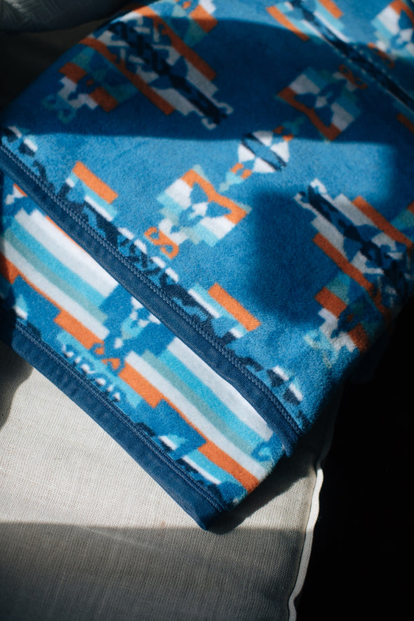 Close up of a corner of the blanket showing a clear pattern and a symbol of a mother holding her child, the body of the mother is a geometric blue shape and the baby is on the inside  in white
