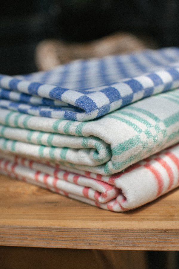 Three checkered blankets stacked folded in dark blue, minty green and red