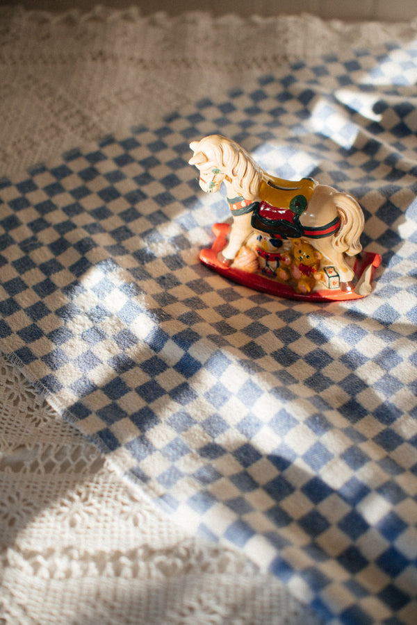 Checkered white and blue blanket on a bed with a rocking horse toy on top